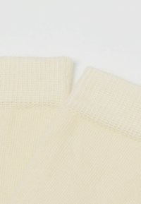 Cremefarvede sokker med ribbet struktur og en glat, vævet crew-manchet. Stoffet ser blødt og åndbart ud, velegnet til hverdagsbrug.