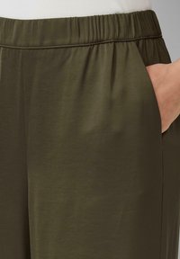 Olivgrüne Hosen mit glatter Textur, elastischem Bund und seitlichen Taschen, entworfen für Komfort und Bewegungsfreiheit.