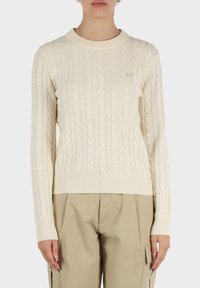 Maglione crema a trecce con scollatura rotonda e polsini a costine. Caratterizzato da un sottile logo sul petto. Texture morbida e forma aderente.