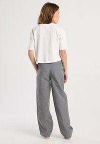 White cropped t-shirt paired with black-and-white checkered wide-leg pants; features short sleeves and a relaxed fit.