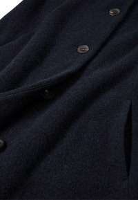 Abrigo de mezcla de lana en un azul marino oscuro, con una textura suave, diseño de doble botonadura y botones redondos y transparentes. Incluye bolsillos laterales visibles.