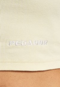 Lys gul ribbet stoff med et brodert "PEGADOR"-logo i hvitt, plassert langs den nedre kanten. Glatt tekstur og tett passform.