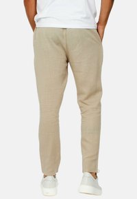 Pantaloni di lino beige slim fit, con tasche laterali e polsini elasticizzati, abbinati a sneakers bianche. Texture liscia e design traspirante.