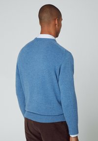 Pull bleu en maille avec un col rond et des poignets côtelés, présentant une texture lisse et une silhouette ajustée.