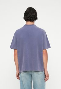 Īsām piedurknēm, brīva piegriezuma t-krekls mīksta lavandas krāsā. Tam ir klasiskas apaļas izgriezums un gluda, neapstrādāta virsma.