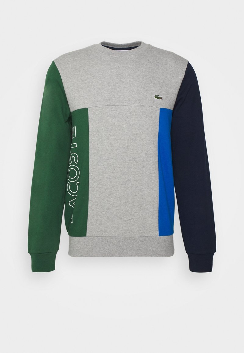 Sweat-shirt gris avec des manches colorées en vert, bleu et marine, finition texturée et logo Lacoste sur le devant.