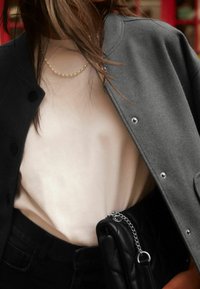 Veste grise boutonnée sur une chemise beige, associée à un jean noir. Complété par un sac à main matelassé noir avec une chaîne argentée.