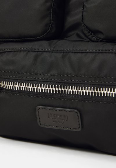 Fekete nylon hátizsák ezüst cipzárral, párnázott dizájnnal és a külső részén varrt bőr Moschino címkével.