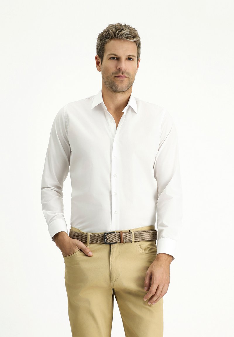 Camicia bianca a maniche lunghe con colletto, abbinata a pantaloni khaki e una cintura intrecciata marrone. Tessuto morbido, vestibilità su misura.