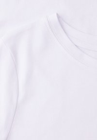 T-shirt blanc en coton avec col ras du cou et coutures doubles au niveau du col et des épaules, montrant la partie supérieure gauche de la poitrine et la manche.