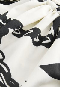 Gros plan sur des formes abstraites noires sur un tissu blanc plissé, montrant la texture et les plis.