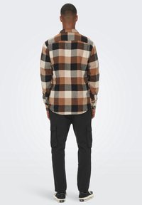 Camisa de franela de cuadros en tonos marrón y crema con detalles en negro; diseño de manga larga, abotonado, con dobladillo curvado y tela texturizada.