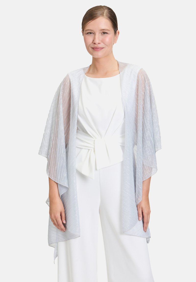 Veste de style kimono argent clair avec une texture transparente et des rayures verticales, portée sur un haut blanc et un pantalon large.