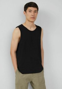Schwarzes ärmelloses Tanktop aus weichem Stoff, mit lockerer Passform und rundem Ausschnitt. Getragen mit hellbeigen Cargo-Hosen.