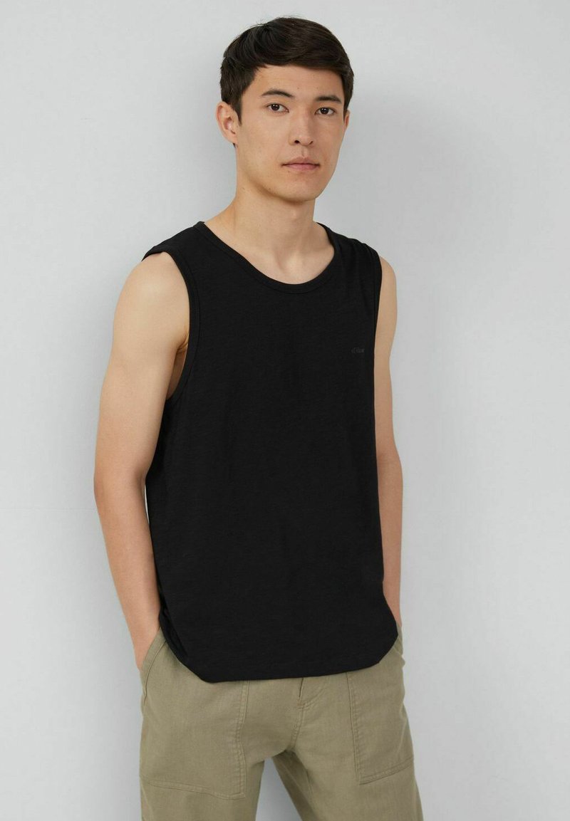 Schwarzes ärmelloses Tanktop aus weichem Stoff, mit lockerer Passform und rundem Ausschnitt. Getragen mit hellbeigen Cargo-Hosen.