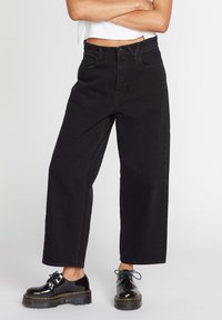 Zwarte wijde spijkerbroeken van denim met een hoge taille, voorzakken en subtiele stiksels, gecombineerd met glanzende zwarte veterschoenen.