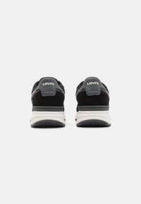 Crne sued sneakers sa sivim detaljima i bijelim srednjim potplatom. Na peti se nalazi bijeli "LEVI'S" brend. Tekstura na površini i složeni dizajn.