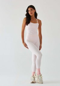 Biały zestaw odzieży sportowej składający się z dopasowanego topu na ramiączkach i legginsów. Noszony z jasnymi sneakersami i różowymi skarpetkami w paski. Gładka faktura.