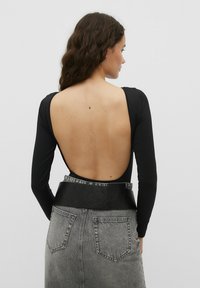 Schwarzer langärmeliger Body mit tiefem Ausschnitt im Rücken, kombiniert mit einem grauen, hoch taillierten Jeansrock mit einem schwarzen, kunstledernen Taillengürtel.