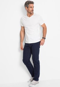 T-shirt bianca con scollo a V, jeans blu scuro e sneaker grigie chiare. Vestibilità slim e design semplice. Senza motivi o accenti aggiuntivi.
