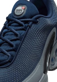 Blue textile sneaker with mesh upper, features circular logo on tongue, and distinct textured design on the side. Transparent sole with air cushion.