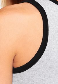 Harmaa tehdyt hihaton paita mustalla reunuksella, jossa on leveät kainalot ja pehmeä kangas, joka korostaa hartioiden ja ylä-olan taustaa.