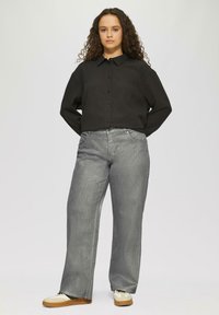 Zwart, knoopshirt met korte mouwen en een gestructureerde stof; gecombineerd met lichtgrijze, wijde jeans. Draagt neutrale sneakers.