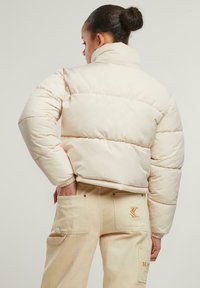 Kremet pufferjakke med høy krage, med heklede seksjoner og elastiske mansjetter, parret med beige cargo bukser som har store lommer.