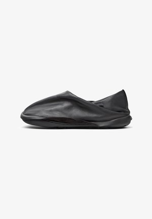 Scarpa nera in pelle, slip-on, con una texture morbida e stropicciata e profilo basso. Presenta una suola flessibile e un design minimalista senza parti metalliche visibili.