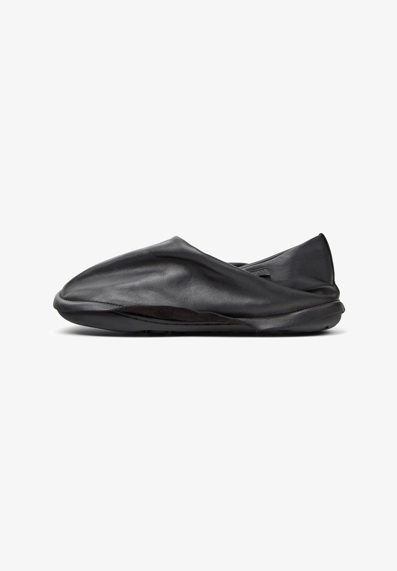 Scarpa nera in pelle, slip-on, con una texture morbida e stropicciata e profilo basso. Presenta una suola flessibile e un design minimalista senza parti metalliche visibili.