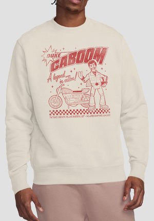Man wearing cream sweatshirt with red graphic of Duke Caboom toy figure and motorcycle, text reads "A legend in action!"