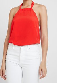 Rode mouwloze haltertop van lichtgewicht stof met een zachte textuur, gecombineerd met hoge taille witte jeans.