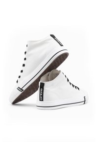 Sneaker alte bianche con lacci neri, etichetta nera e suola in gomma. Materiale in tela e design semplice con accenti in contrasto.