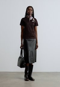 Melna īsroku krekls, pieguļoša brūnas ādas midi svārki un brūnas zābaki līdz ceļiem. Aksesuārs: rakstains lakats. Melna soma.