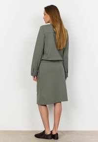 Olijfgroene twee-delige outfit met een lange mouw top met een ontspannen pasvorm en een jurk tot op de knie. Glad materiaal met een elastische tailleband.
