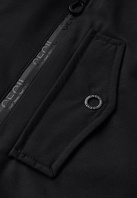 Veste noire avec fermeture éclair sur le devant et panneau transparent. Comprend une poche à rabat et un accent de logo circulaire. Texture de tissu lisse.