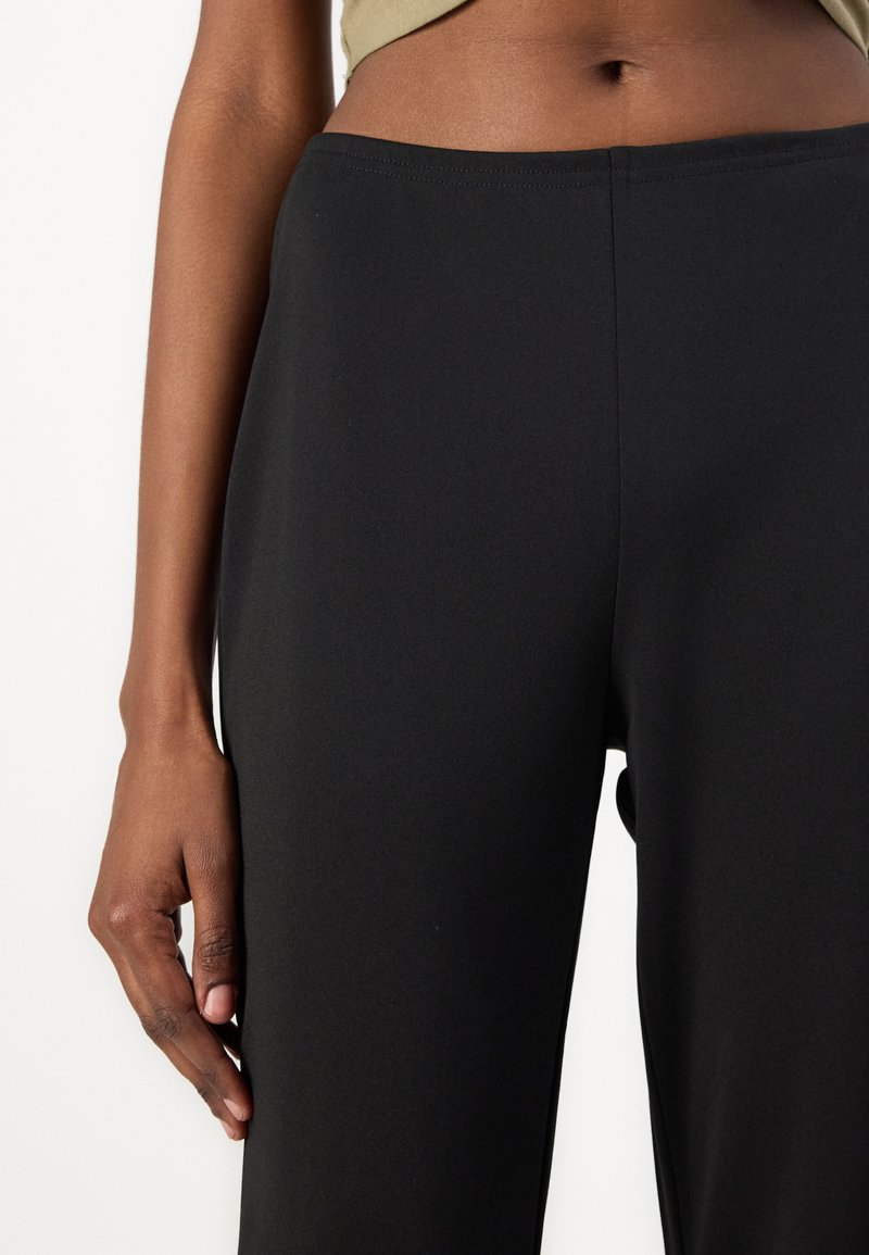 Schwarze High-Waist-Leggings aus dehnbarem Stoff. Sie haben eine glatte Textur und eine enganliegende Silhouette, mit einem breiten Bund.