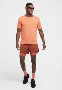 Conjunto deportivo de Nike que incluye una camiseta naranja de manga corta y pantalones cortos rojos. Los accesorios incluyen gafas de sol con tintado naranja y zapatillas de correr negras.
