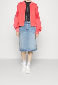 Sudadera coral con cuello redondo y hombros caídos, combinada con una falda midi de denim azul claro y zapatillas blancas con detalles texturizados.