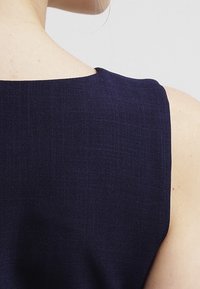 Navy blue ilman hihoja oleva mekko, jossa on rakenteellinen kaula-aukko, valmistettu teksturoidusta kankaasta, sisältäen siistejä linjoja ja minimalistisen muotoilun.