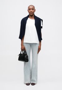 Borsa nera, t-shirt grafica bianca, cardigan blu navy drappeggiato sulle spalle, jeans svasati azzurri e scarpe bordeaux. Texture lisce in tutto.