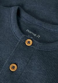 Dark blue ribbed sweater featuring a round neckline, wooden buttons, and textured fabric. Brand label "name it" visible near collar.