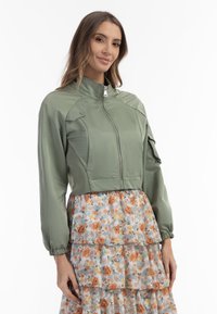 Olivengrøn cropped jakke med lange ærmer, høj krave og lynlås. Har teksturerede paneler og er designet til en tætsiddende pasform.