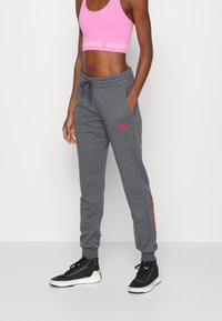 Grå joggingbukser med rødt Adidas-logo, elastisk taljebånd og manchetter, kombineret med en lyserød kort sports-bh. Sorte træningssko fuldender looket.