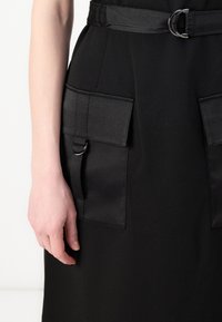 Black dress featuring a satin texture with two large side pockets, a belt with a metallic buckle, and a form-fitting silhouette.