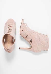 Sandalias de tacón en rosa empolvado con diseño recortado, adornadas con rhinestones y cierre de cremallera en la parte posterior. Fabricadas en suave material de ante.