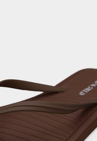 Καφέ σαγιονάρα με υφή στο πέλμα και λεπτά λουράκια, λοξή όψη σε λευκό φόντο.