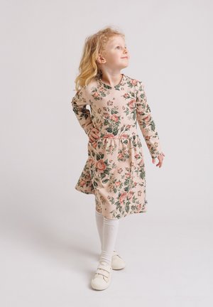 Sukienka w kwiaty z miękkiego różowego materiału, z długimi rękawami, okrągłym dekoltem, marszczonym taliowaniem, ozdobiona zielonymi i brzoskwiniowymi kwiatami. Do tego białe podkolanówki i buty.