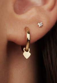 Gold hoop earring featuring a heart-shaped charm, smooth finish; paired with a small gold stud with a clear gemstone accent.
