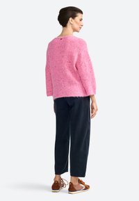 Maglione rosa a maglia con maniche tre quarti, caratterizzato da una texture a anello. Abbinato a jeans scuri e sneakers marroni.